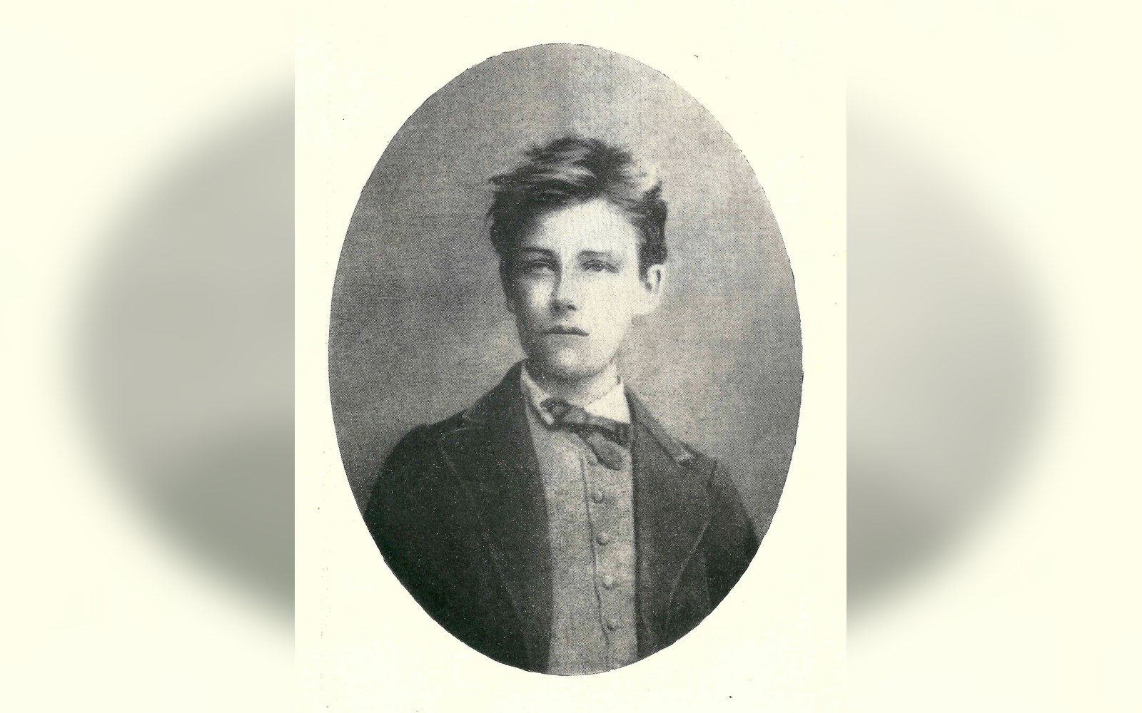 Vintage oval portrait of a young man with tousled hair, wearing a bow tie and jacket